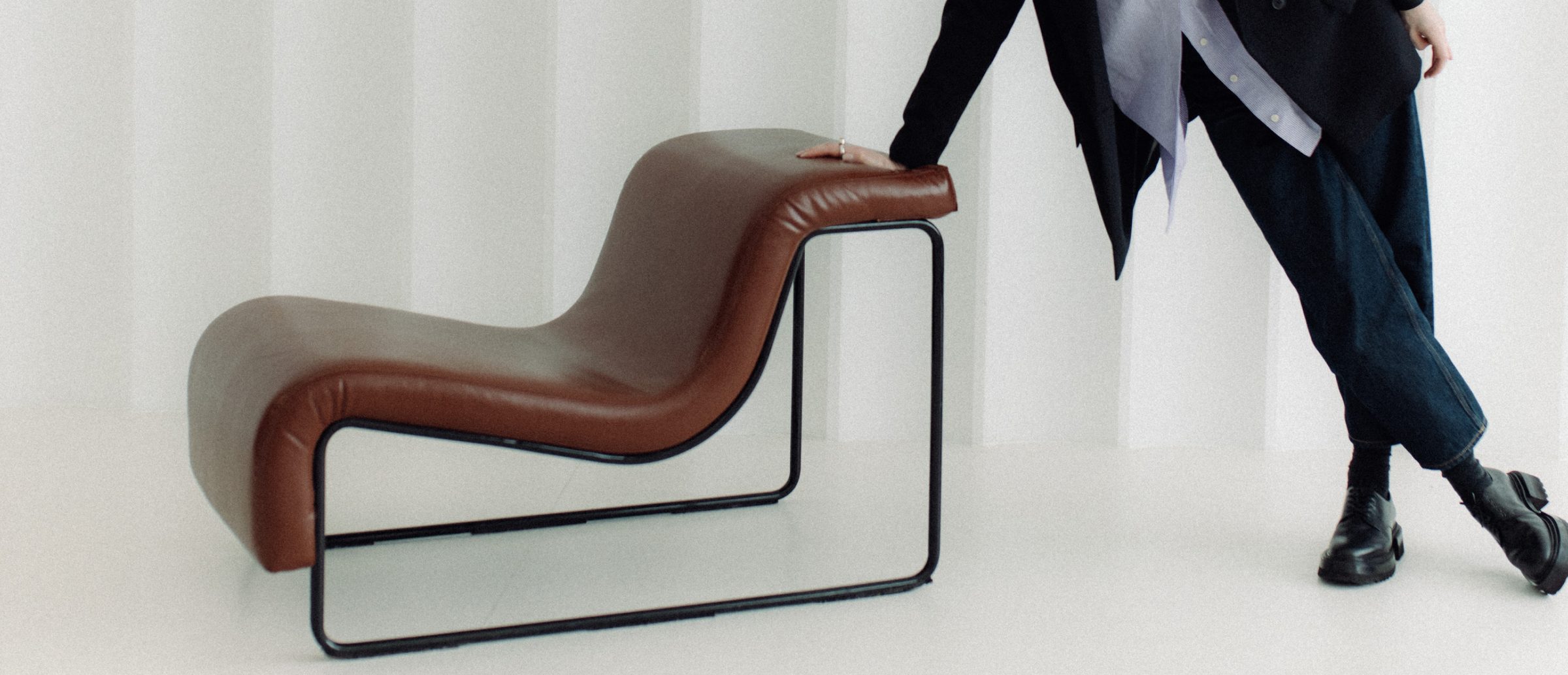 A leather lounge chair in a white studio, Ilona leaning on it